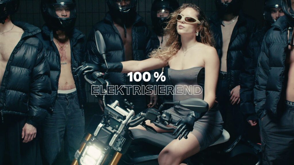 Eli Preiss sitzt selbstbewusst auf E-Motorrad in Szene mit Models in schwarzen Jacken und dem Claim 