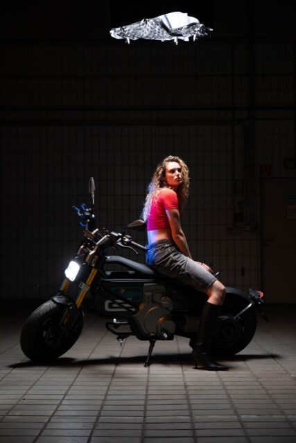 Eli Preiss sitzt im Spotlight auf einem E-Motorrad in einer dunklen Halle als Teil der visuellen Digitalkampagne