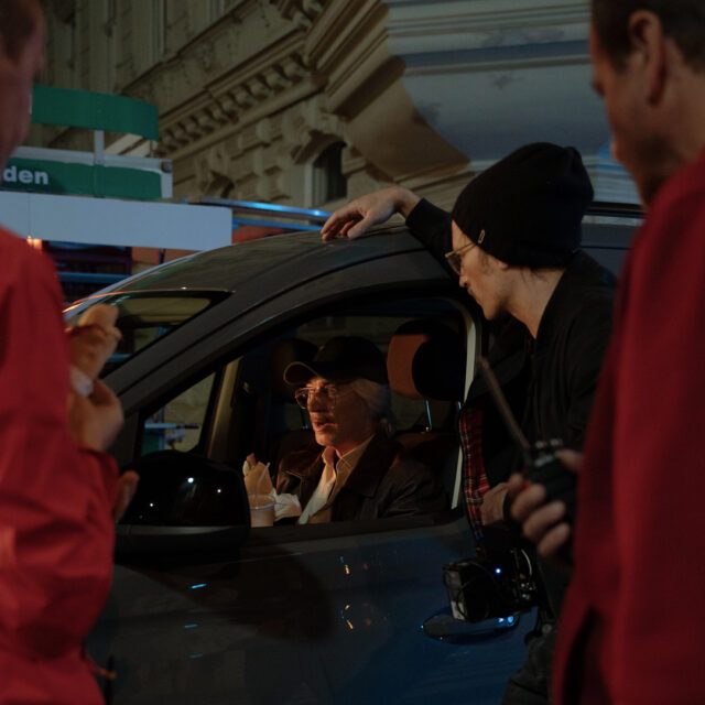 Behind-the-scenes Moment am Filmset mit Schauspieler im Fahrzeug und Crew in nächtlicher Stadtatmosphäre, produziert von Wuger
