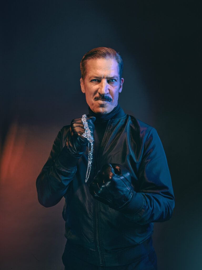 Porträt von Moretti als Dieb in dunkler Kleidung mit dramatischer Lichtstimmung und Accessoire in der Hand