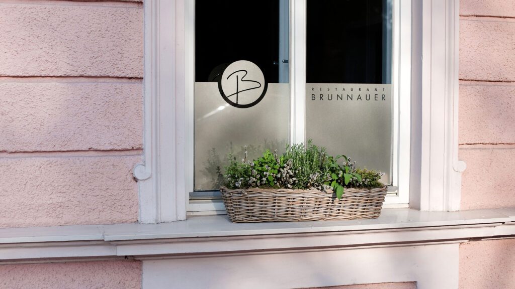 Branding am Fenster des Restaurants Brunnauer mit stilisiertem Logo und Kräuterkasten, Teil unseres Corporate Design Gastronomie Projekts von Wuger