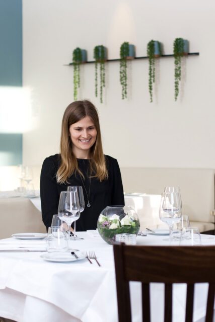 Gästin im Restaurant Brunnauer sitzt an elegant gedecktem Tisch mit Blumenschale, fotografiert für unser Corporate Design Gastronomie Projekt