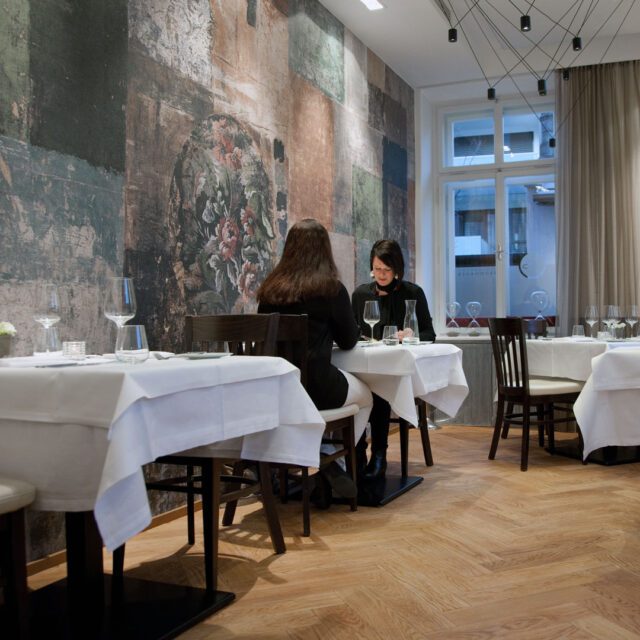 Restaurant Interior Brunnauer mit floraler Wandgestaltung und zwei Gästen, fotografiert für unser Corporate Design Gastronomie Projekt und den Corporate Design Case von Wuger