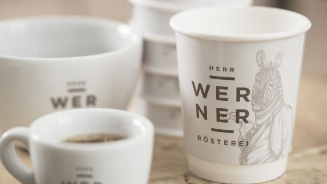 Nahaufnahme bedruckter Kaffeebecher und Tassen mit illustrativem Branding als Teil des Packaging Designs umgesetzt von Wuger