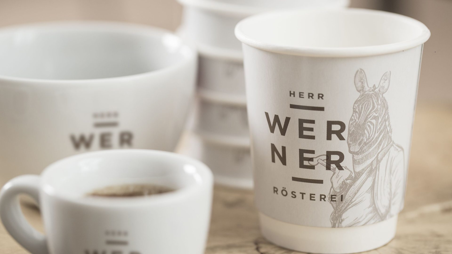 Nahaufnahme bedruckter Kaffeebecher und Tassen mit illustrativem Branding als Teil des Packaging Designs umgesetzt von Wuger
