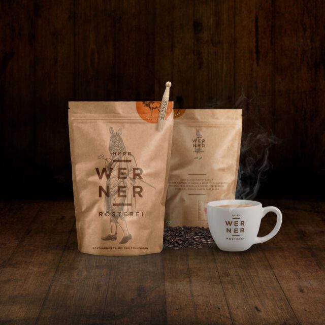 Kaffeepackungen und dampfende Tasse auf Holzboden als atmosphärische Produktvisualisierung im Packaging Design umgesetzt von Wuger