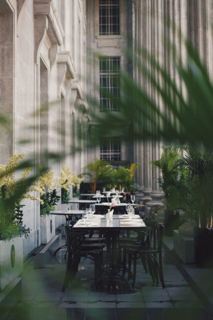 Hotelterrasse mit elegant gedeckten Tischen zwischen Steinsäulen und Pflanzen – Teil des HOGAST Rebranding Projekts von WUGER Hospitality zur Inszenierung moderner Gastfreundschaft.