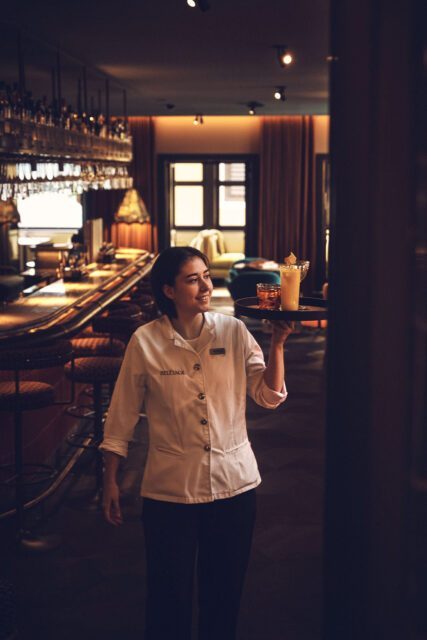 Servicemitarbeiterin serviert Drinks an der Hotelbar – Teil der HOGAST Bildwelt, fotografiert im Rahmen des Rebrandings durch WUGER.