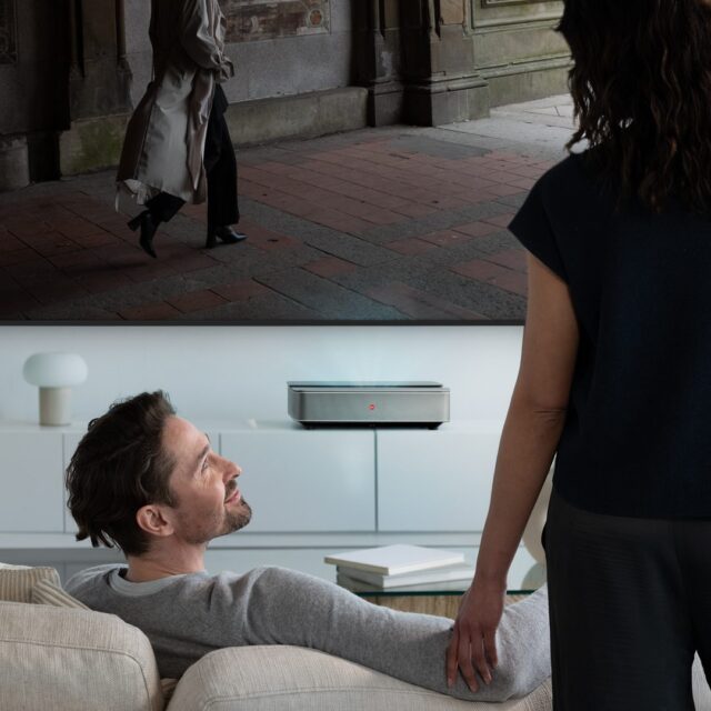 Ein Mann sitzt entspannt im Wohnzimmer und blickt auf eine Projektion des Leica Cine 1, der ein filmisches Bild an die Wand wirft – stilvolle Home-Cinema-Inszenierung von WUGER.