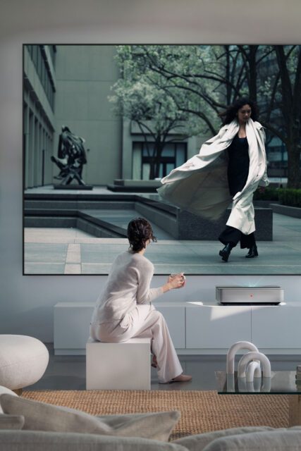 Eine Frau sieht sich eine Filmszene an, projiziert vom Leica Cine 1 im hellen Wohnzimmer. Premium-Kampagne von WUGER.