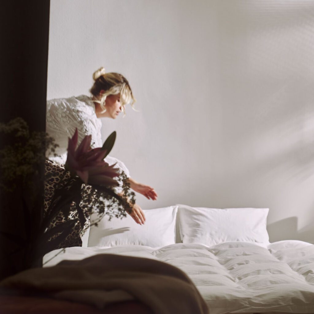 Frau richtet ein Bett in einem hellen Zimmer des Stiegnhaus, fotografiert für das Corporate Design Boutique Hotel Projekt und die Darstellung des Service