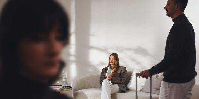 Die Szene mit ankommenden Gästen spiegelt das Erlebnis im Stiegnhaus wider. Im Corporate Design Boutique Hotel Case fangen wir solche Momente ein. Szene in der Lobby des Stiegnhaus: Frau mit Notizbuch auf dem Sofa und Mann mit Koffer, Teil unseres Corporate Design Boutique Hotel Projekts