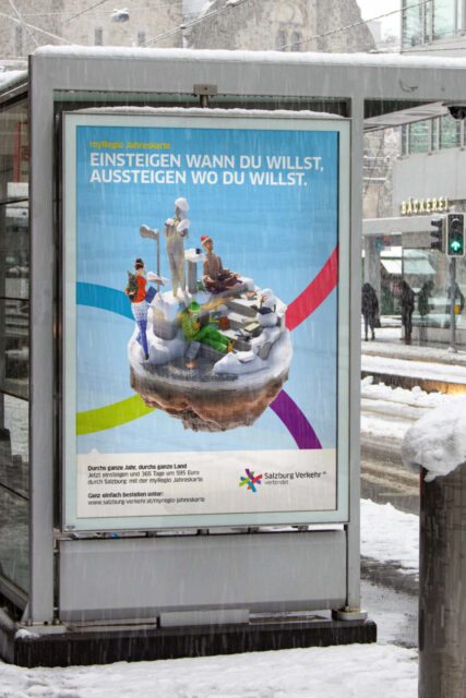 Plakat von Salzburg Verkehr an einer verschneiten Haltestelle mit 3D Figuren auf einer kleinen Insel und dem Slogan 