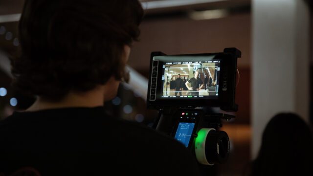 Blick über die Schulter auf einen Regiemonitor mit laufender Szene, festgehalten vom Filmteam von Wuger