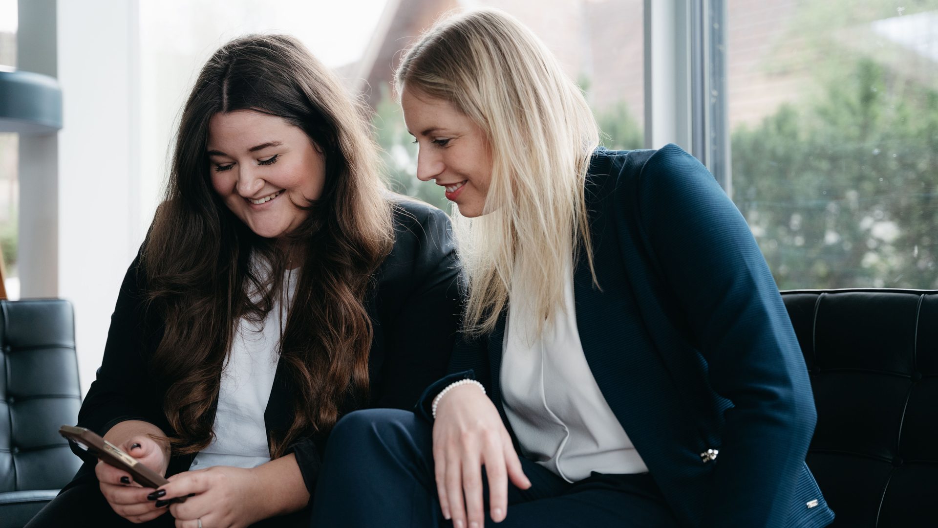 Zwei Personen sitzen auf einem Sofa und betrachten gemeinsam ein Smartphone während einer Besprechung zur Digitalstrategie
