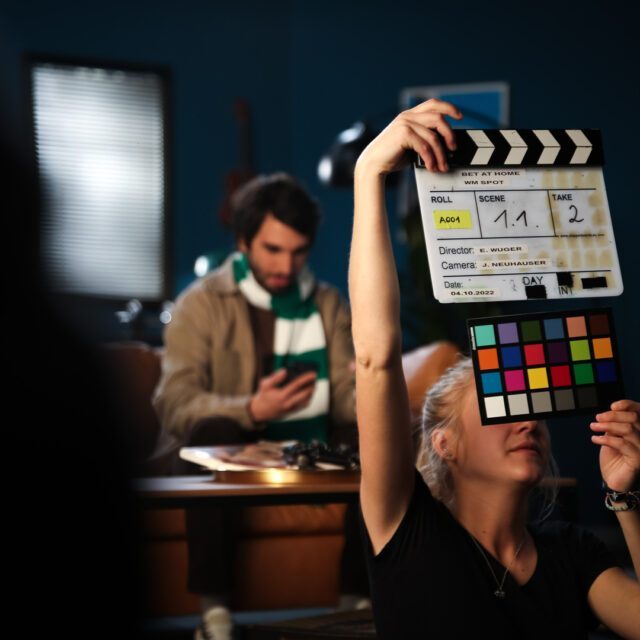 Wuger Teammitglied hält bei Shooting die Filmklappe, im Hintergrund die Darsteller