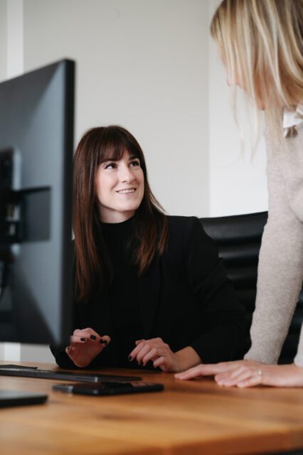 Wo Ideen entstehen und Zusammenarbeit zählt. Zwei Mitarbeiterinnen der Full Service Werbeagentur Wuger in Salzburg im Gespräch am Arbeitsplatz über kreative Marketingstrategien