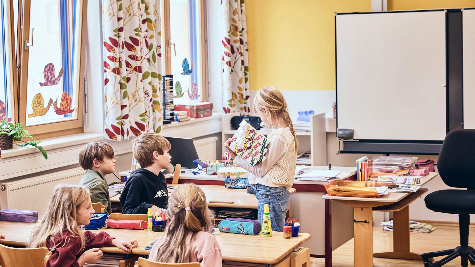 Präsentieren und Mitmachen im Unterricht verankern Mobilität über gemeinsames Lernen. Foto zeigt Kinder im Klassenzimmer beim Austeilen der Entdeckerboxen, mit denen Wuger Event Marketing erlebbar macht
