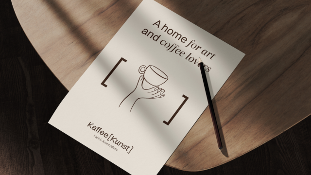 Weißer Flyer mit Logo von Kaffee Kunst auf Holztisch, fotografiert von Wuger als Teil eines stimmigen Brandings