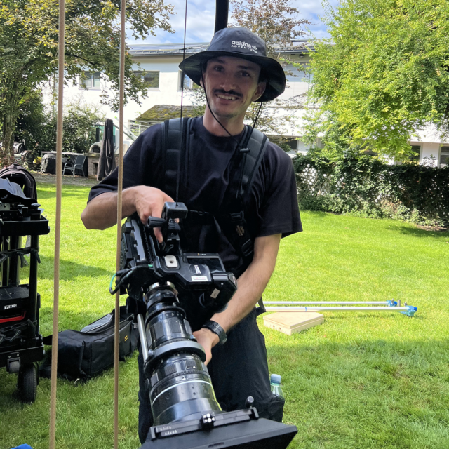 Behind-the-Scenes einer Imagefilm- und Fotoproduktion, bei dem Kameramann professionelle Filmkamera auf Außenset hält