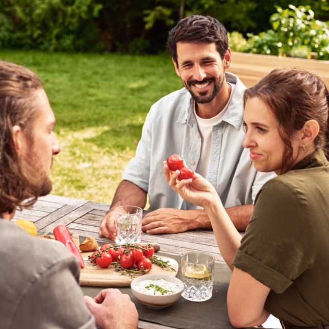 Drei Personen sitzen im Garten mit frischem Gemüse und lachen, emotionales Lifestyle-Imageshooting für eine Gartenmarke