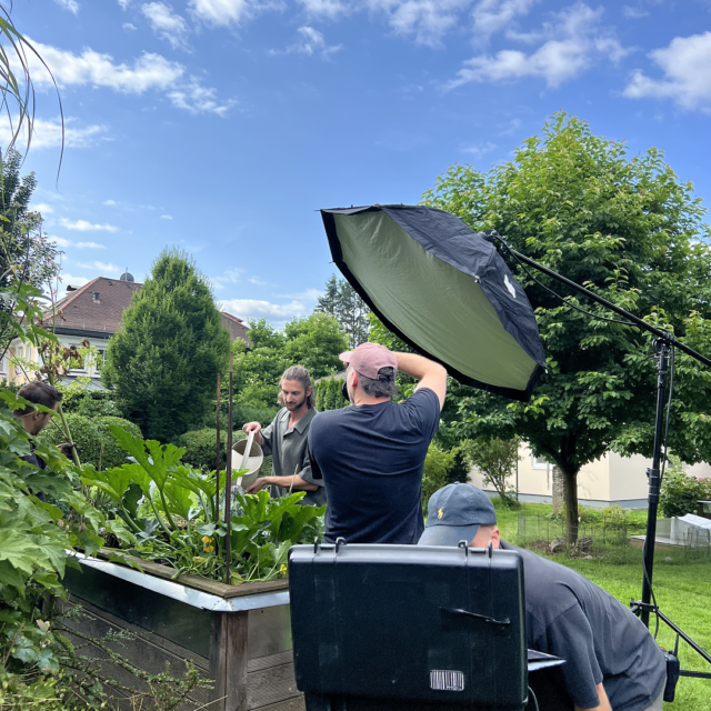 Fotograf richtet Softbox auf Model am Hochbeet aus, Behind-the-Scenes eines professionellen Imagefilm- und Fotoshootings im Freien