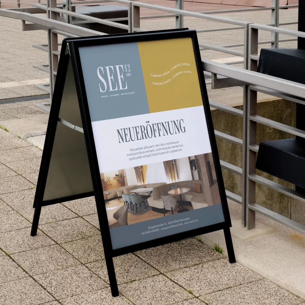 Direkt vor der Tür macht der Aufsteller neugierig auf das, was drinnen bald serviert wird. Aufsteller mit Neueröffnungsplakat und Interieurbild auf dem Gehweg als Kampagne und Corporate Design von Wuger vor dem Lokal