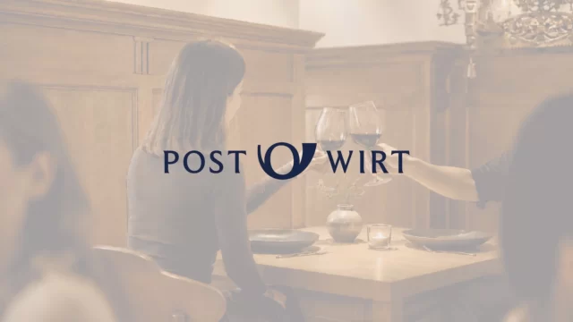 Neu entwickeltes Logo für bayerisches Businesshotel vor warmem Gaststuben-Ambiente mit anstoßendem Paar