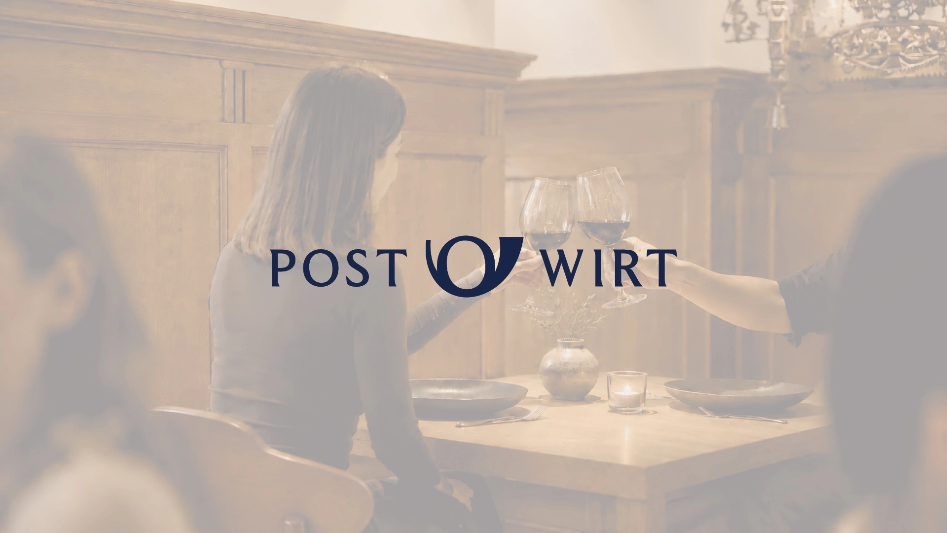 Neu entwickeltes Logo für bayerisches Businesshotel vor warmem Gaststuben-Ambiente mit anstoßendem Paar