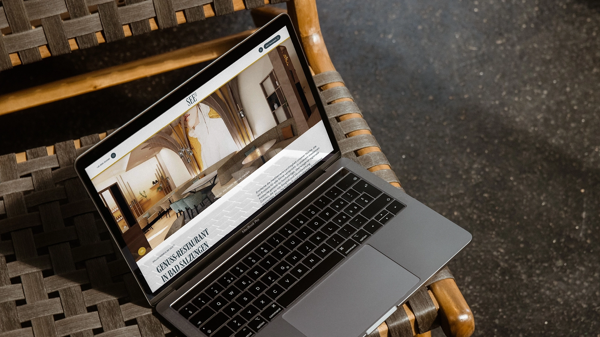 Auch am Bildschirm bereitet das SEE12 schon einen warmen Empfang. Laptop auf Flechtstuhl zeigt die Restaurant-Website als Corporate Design und Digital Marketing von Wuger mit Interieurbild